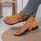 Model's feet wearing Rhyzak women's orange faux-leather flat sandals with a toe loop and adjustable ankle strap, styled with denim jeans on a textured woven mat.