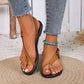 Model's feet wearing Rhyzak women's flat thong sandals in tan faux leather with a toe loop and adjustable buckle ankle strap, styled with denim jeans and a turquoise anklet on a woven mat.