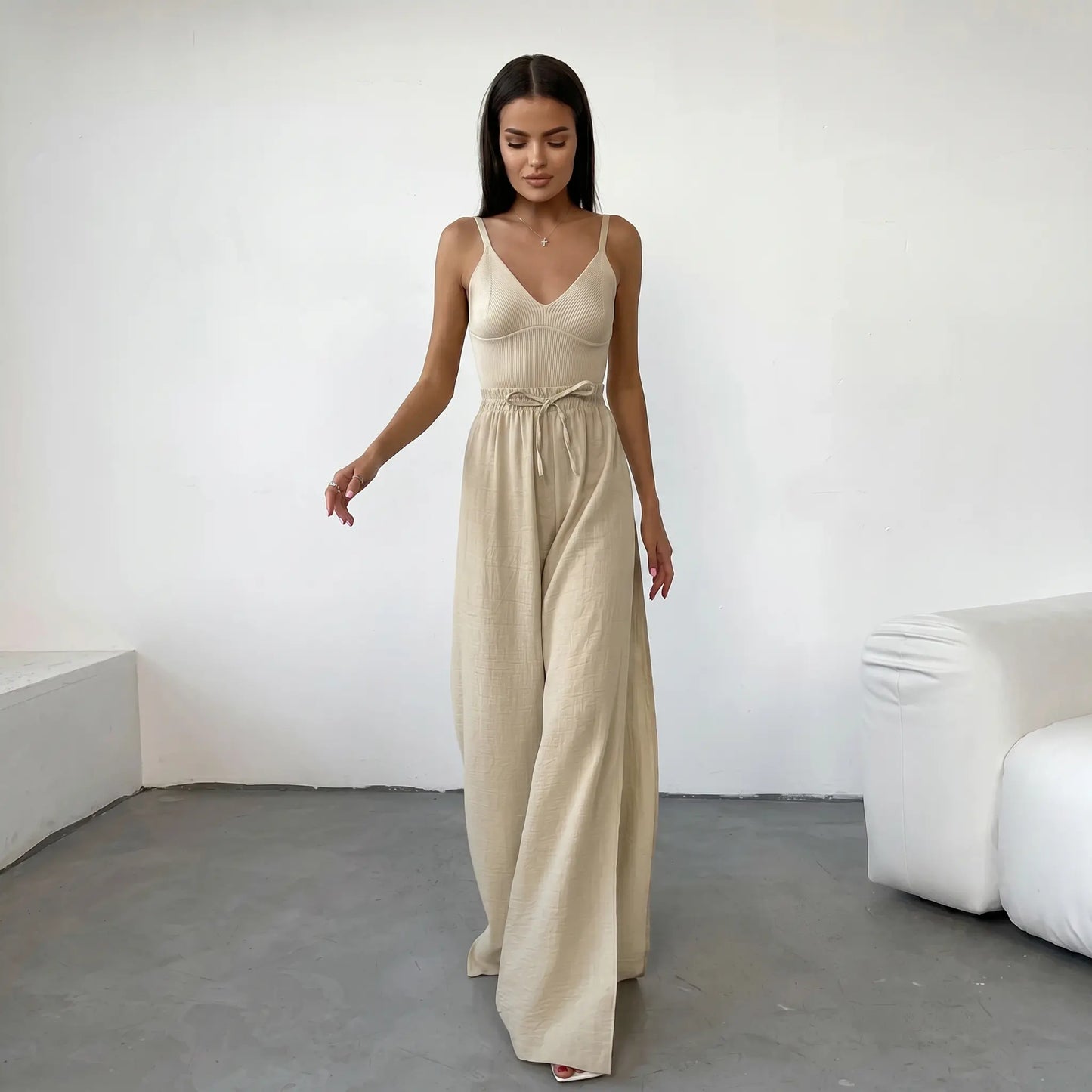 Rhyzen high-waisted wide-leg trousers in textured oat-beige breathable cotton, worn by a model with deep side slits and a drawstring waist. Shot from the front in a studio.