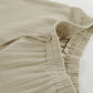 Close-up of Rhyzen wide-leg trousers showcasing the breathable slubbed oat-beige cotton fabric, elasticated waistband, and natural drawstring detail.