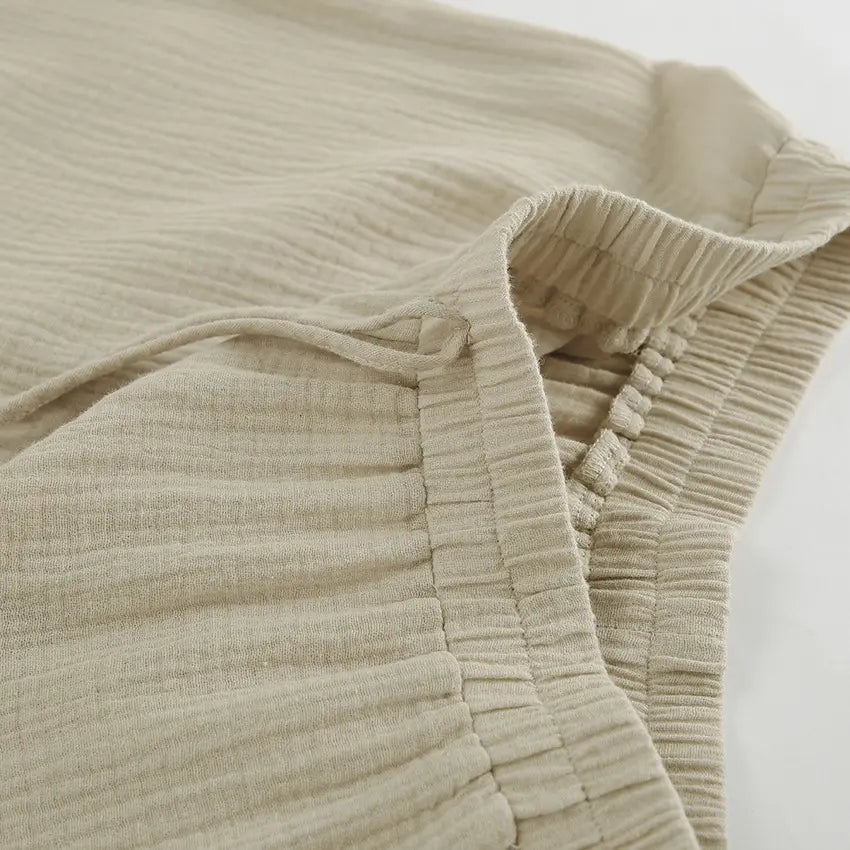 Close-up of Rhyzen wide-leg trousers showcasing the breathable slubbed oat-beige cotton fabric, elasticated waistband, and natural drawstring detail.