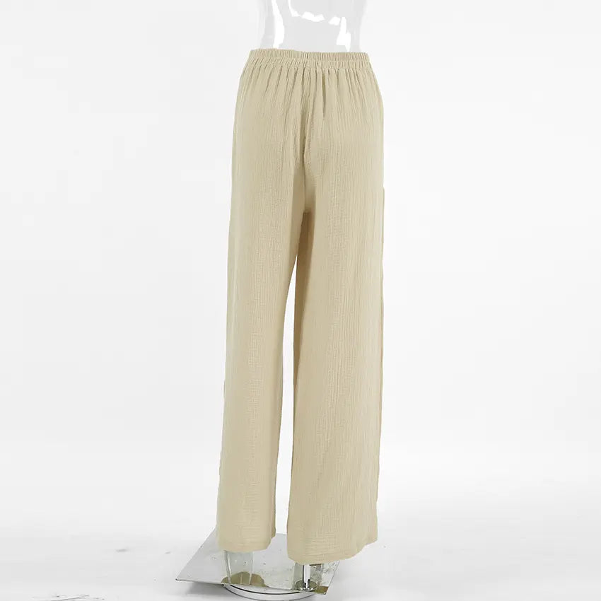 Back view of Rhyzen high-waisted, wide-leg trousers in a textured oat-beige breathable cotton fabric, featuring deep side slits and a flat drawstring waist.
