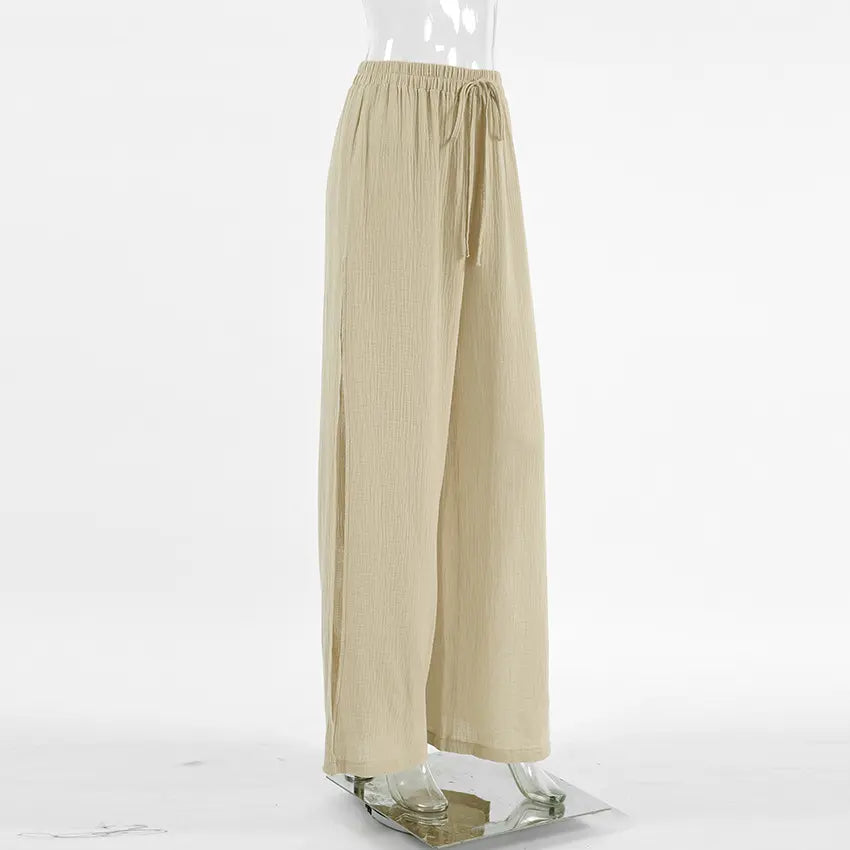 High-waisted, wide-leg trousers in textured oat-beige slubbed cotton, shown from a side view with deep thigh slits and a drawstring waist.