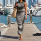 Model in Zyphron Midnight Black sleeveless ribbed knit maxi dress with horizontal black and white stripes, walking on a pier with yachts in the background.