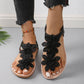 Black Rishka bohemian flat sandals adorned with intricate lace-like floral appliques on the toe strap and a flexible elasticated heel strap, shown on a model's feet.