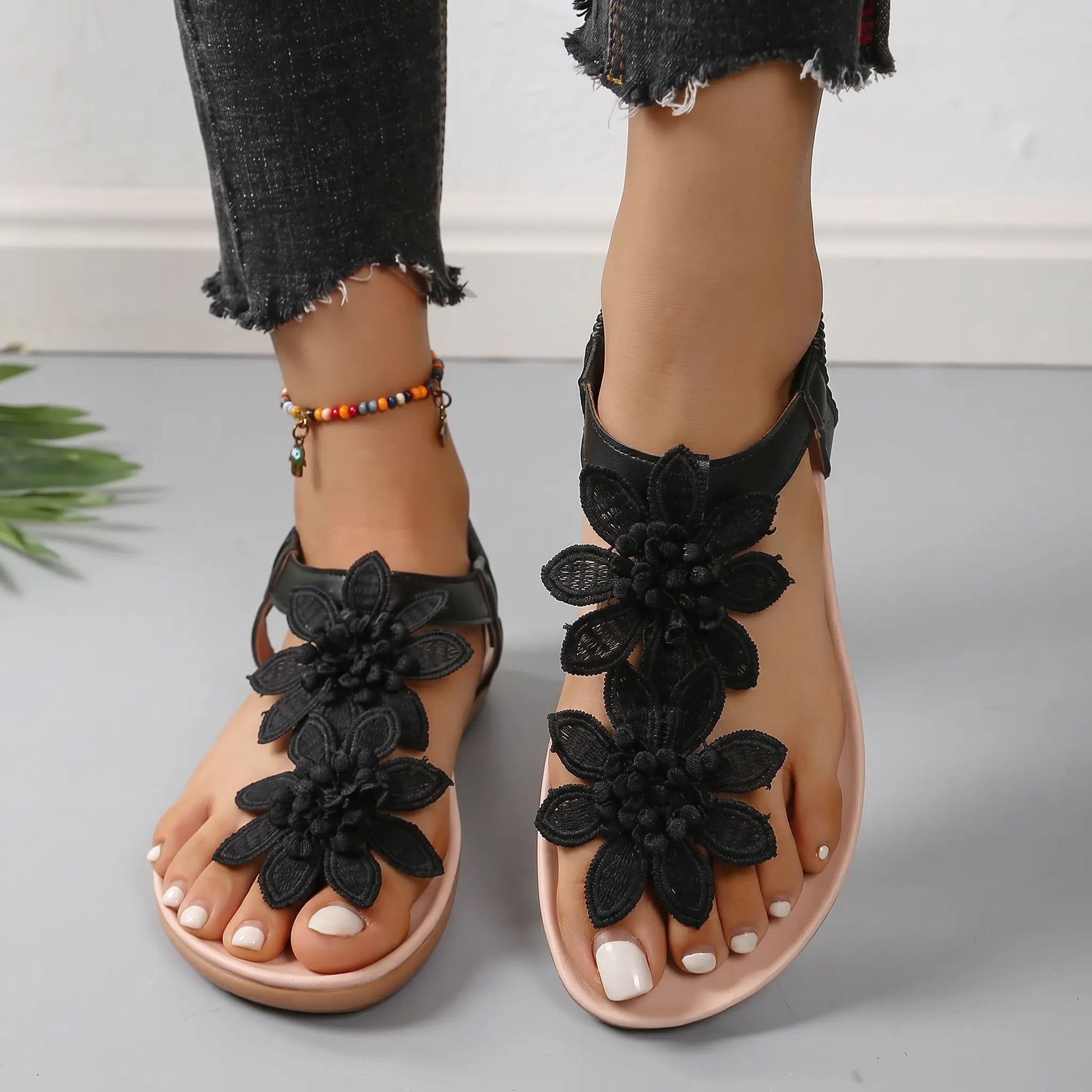 Black Rishka bohemian flat sandals adorned with intricate lace-like floral appliques on the toe strap and a flexible elasticated heel strap, shown on a model's feet.