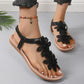 Close-up of a woman's feet wearing Rishka black bohemian flat sandals adorned with layered floral appliques and a black elasticated heel strap.