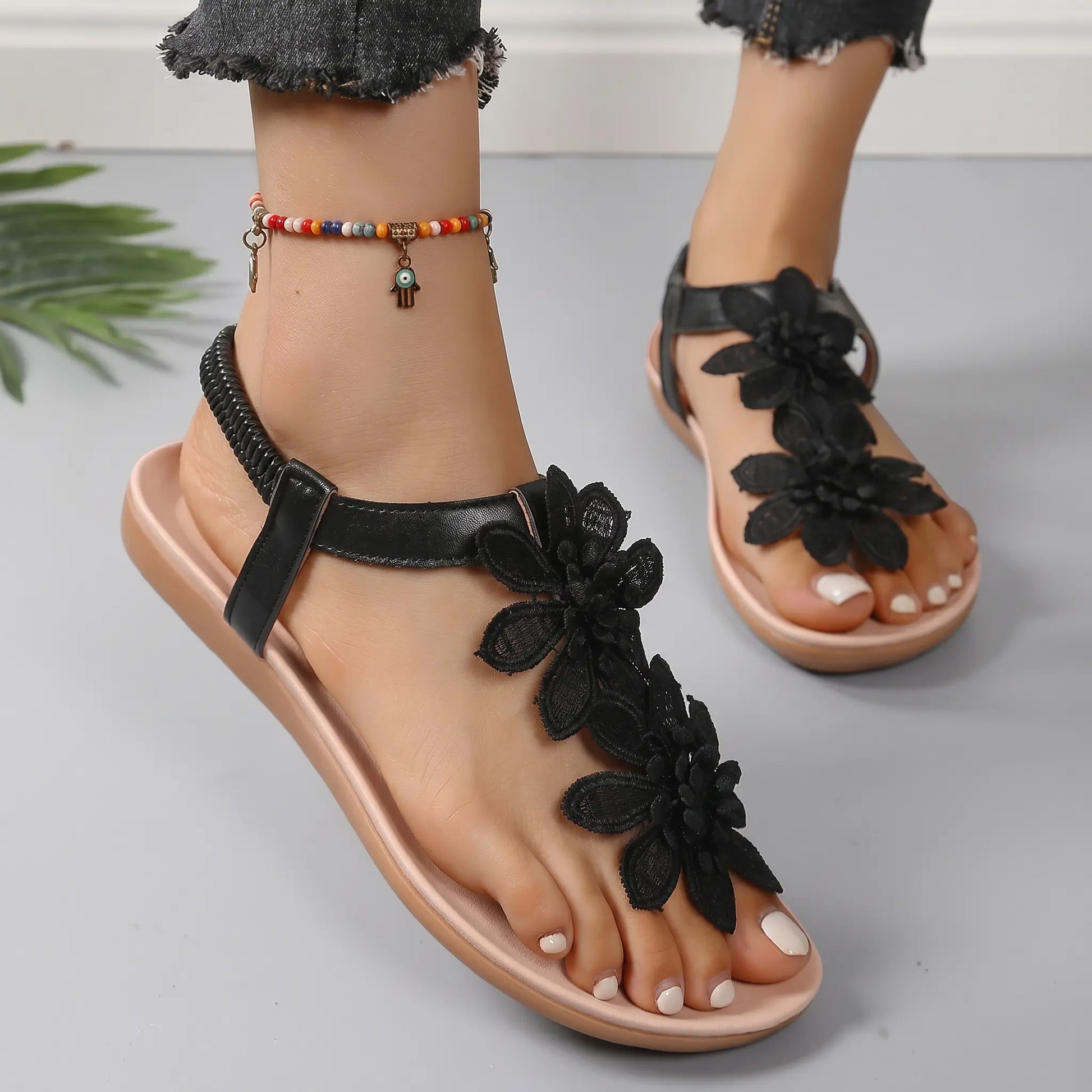 Close-up of a woman's feet wearing Rishka black bohemian flat sandals adorned with layered floral appliques and a black elasticated heel strap.