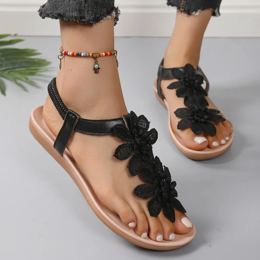 Close-up of a woman's feet wearing Rishka black bohemian flat sandals adorned with layered floral appliques and a black elasticated heel strap.