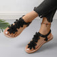 Rishka black bohemian flat sandals adorned with delicate floral appliques on the toe strap and a comfortable elasticated heel strap, showcased on a woman's feet with jeans and a beaded ankle bracelet.