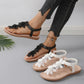 Rishka bohemian flat sandals with black floral appliques on the toe strap and a black elastic heel strap, shown on a model's foot alongside white floral variant pairs.