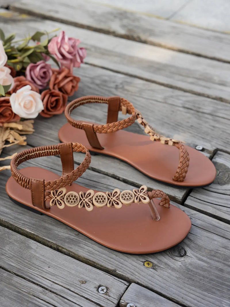 Rivenia Bohemian woven flat sandals in warm brown, featuring a T-strap with carved wood-effect floral and circular embellishments and an elasticized ankle strap.