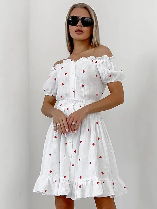Front view of a white off-shoulder RIZUNA dress with a red heart print, ruffled neckline and hem, puff sleeves, and white button-down front.