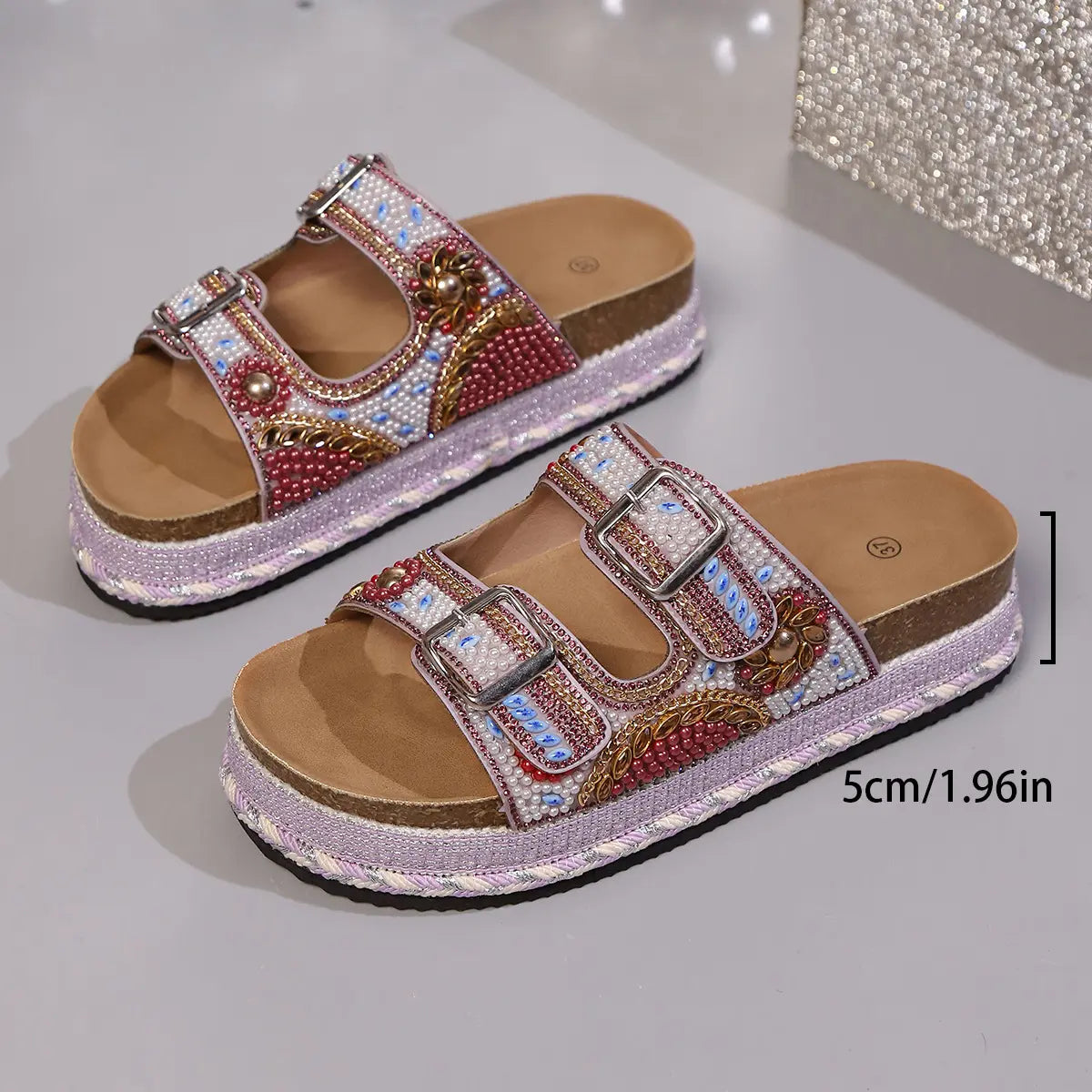 Embellished platform slide sandals in rose pink, featuring double adjustable straps adorned with intricate beads and sequins, a cork-effect platform sole with braided trim, and polished silver buckle hardware.