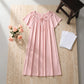 Rosewater Pink Zevryn Romantic Lounge Dress, presented flat-lay, featuring a gathered scoop neckline with a delicate self-tie bow, short flutter sleeves, and a subtle micro-heart pattern, styled on a textured beige surface with pink roses.