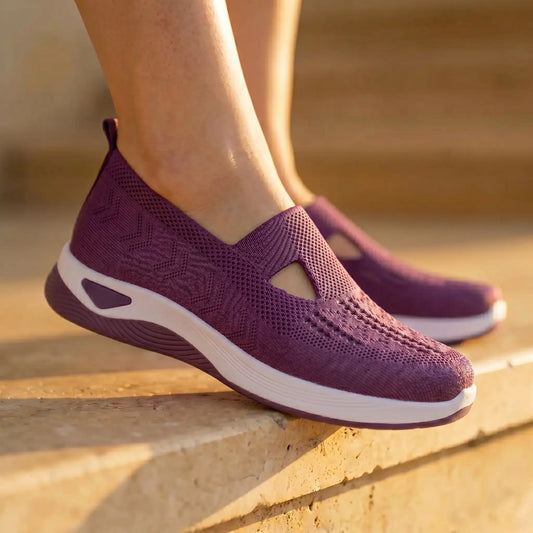 Amethyst purple Ruxen slip-on sneakers worn by a person on sunlit stone steps, showcasing the breathable woven knit upper with diamond perforations and triangular cutout, atop a white platform sole.
