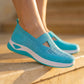 Ocean Cyan Ruxen knit slip-on sneakers with a triangular instep cutout and diamond perforations, worn on feet on sunlit stone steps. The shoes feature a contrasting white sole.