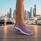 Person wearing Ruxen purple woven knit slip-on sneakers with white soles, walking on a wooden dock at a city marina during sunset.