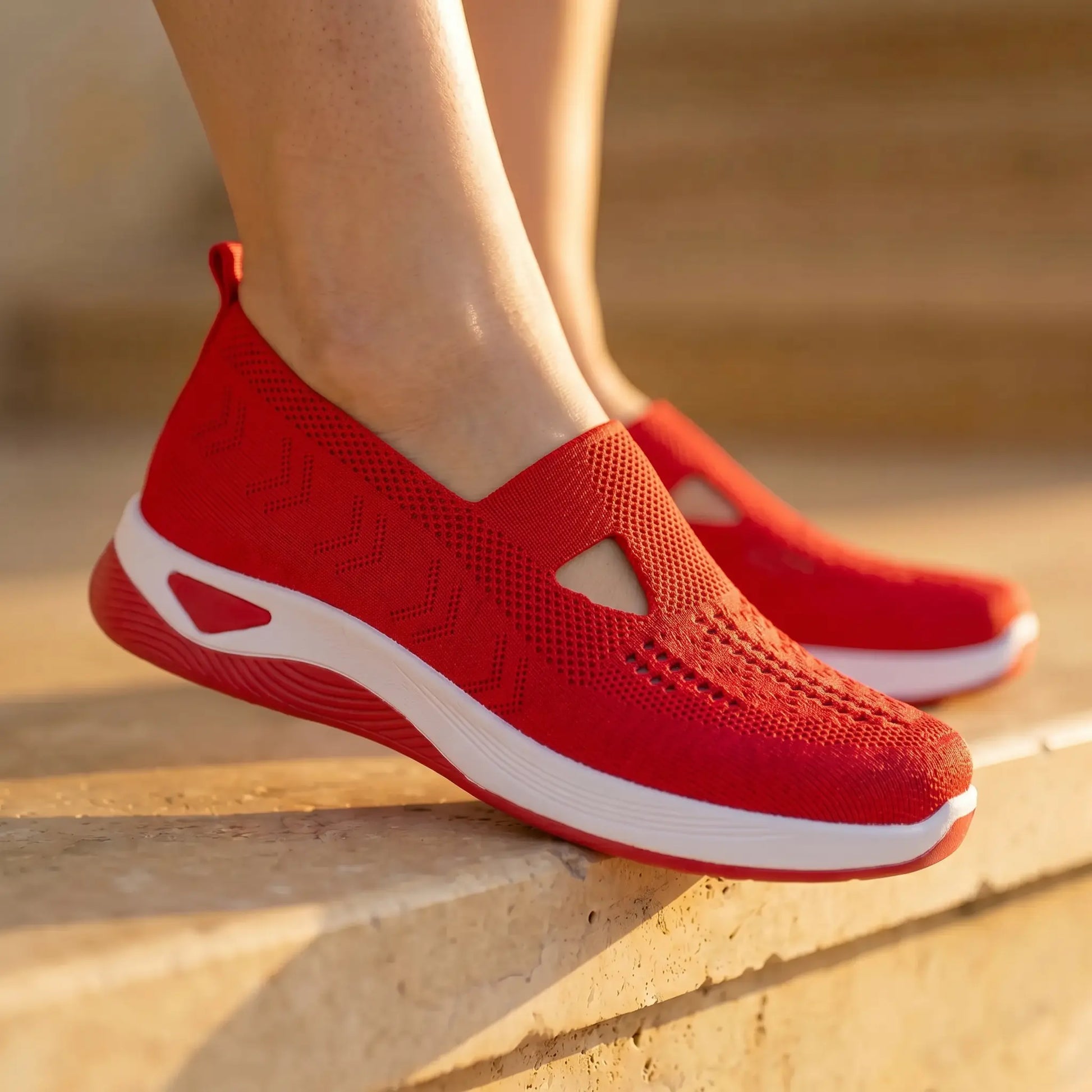 Ruxen Classic Red slip-on sneakers with breathable woven knit and triangular instep cutout, worn on sunny outdoor steps.