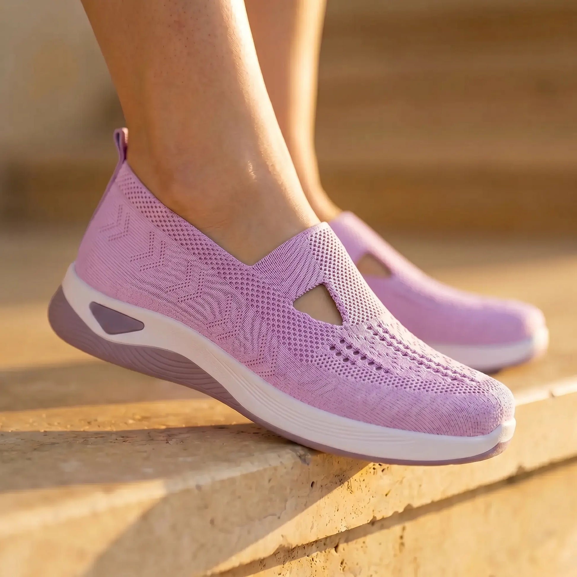 Soft lavender Ruxen slip-on sneakers, showcasing the breathable woven knit with diamond perforations and triangular instep cutout, on sunlit outdoor steps.