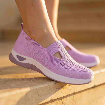 Soft lavender Ruxen slip-on sneakers, showcasing the breathable woven knit with diamond perforations and triangular instep cutout, on sunlit outdoor steps.
