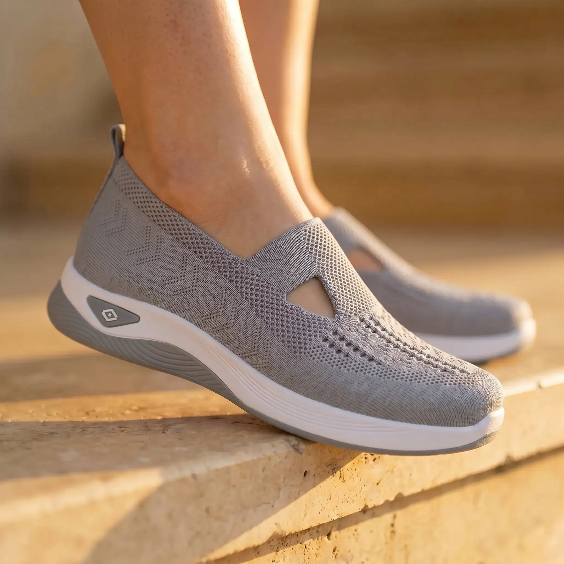 Ruxen Cloud Grey women's slip-on knit sneakers on feet, showcasing the breathable woven upper with triangular instep and white sole, outdoors on steps.