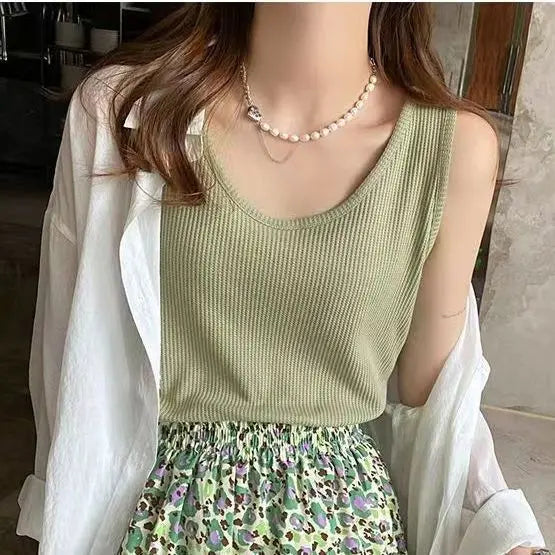 Sage green ribbed knit sleeveless camisole on a model, layered under an open white shirt, accessorized with a pearl necklace.