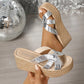 Silver cracked metallic espadrille wedge sandals with criss-cross straps, shown from a three-quarter angle with one sandal on a foot and another in hand.