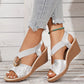 Silver metallic floral print peep-toe wedge sandals with criss-cross elastic straps and a decorative gold-tone ring, worn with casual jeans.