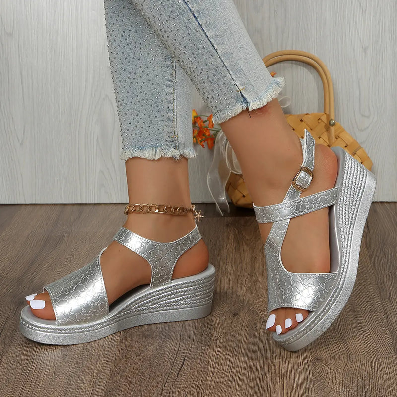 Silver metallic peep-toe wedge sandals with an embossed crocodile texture, worn by a model with distressed denim jeans featuring frayed hems, showcased on a wooden floor.