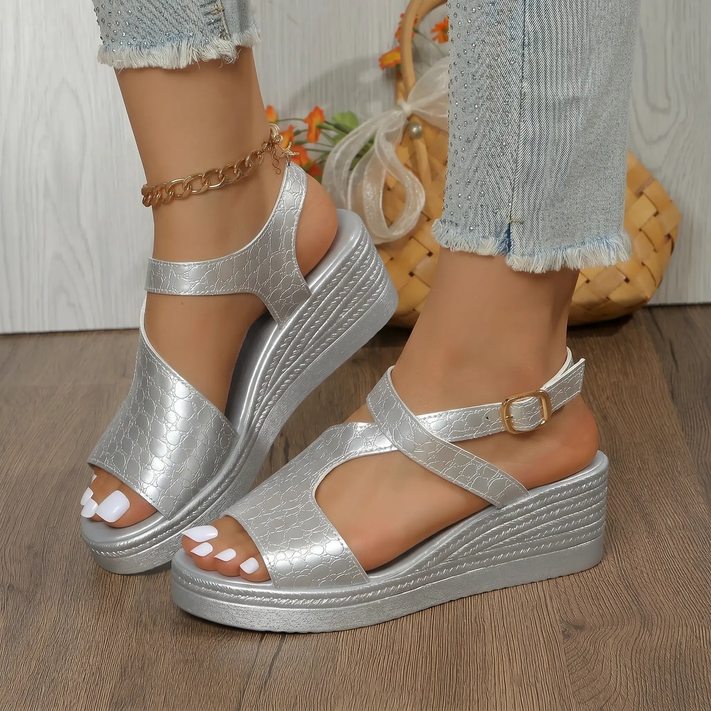 Silver metallic peep-toe wedge sandals with embossed crocodile texture, T-strap, and adjustable ankle strap, worn with distressed jeans on a wooden floor.