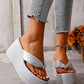Close-up of women's shimmering silver metallic wedge platform flip-flops with a knotted toe strap, worn on feet with distressed denim jeans.