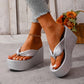 Women's shimmering silver metallic wedge platform flip-flops with a knotted toe strap and woven-textured wedge base, shown on feet from a three-quarter angle with a subtle studio background.