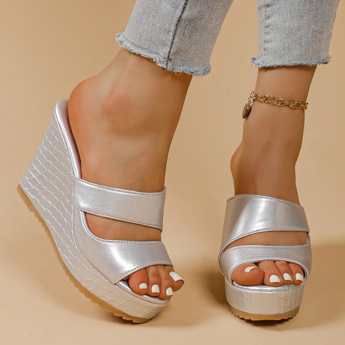 Silver peep-toe platform wedge sandals with intersecting straps worn by a person, showcasing the snake-effect textured wedge and platform.