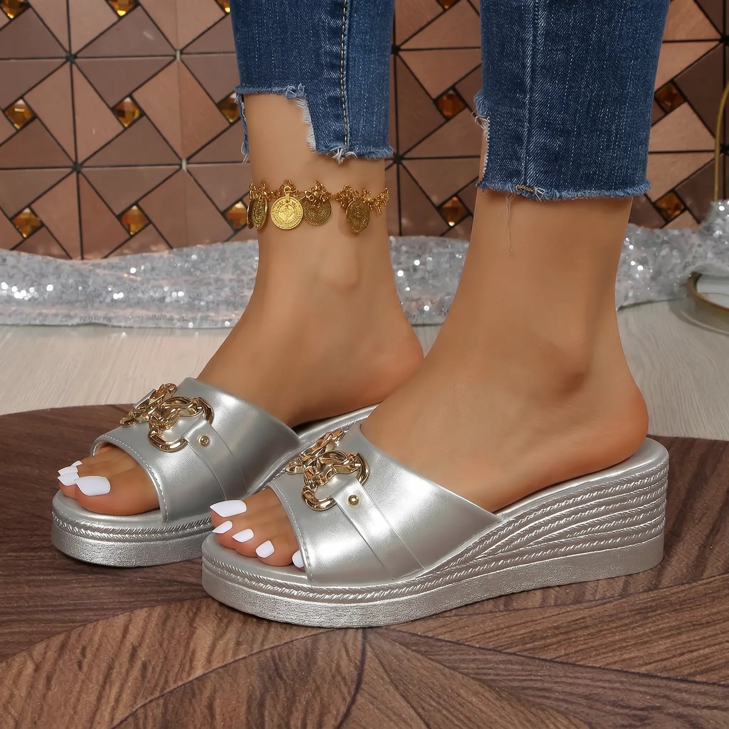 Sterling silver platform wedge sandals featuring a woven heel texture and ornate gold chain embellishment on the single vamp strap, worn with blue jeans.