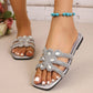 Close-up of silver flat slide sandals adorned with sparkling floral rhinestone embellishments on a model's feet, showcasing the square toe and comfortable design.