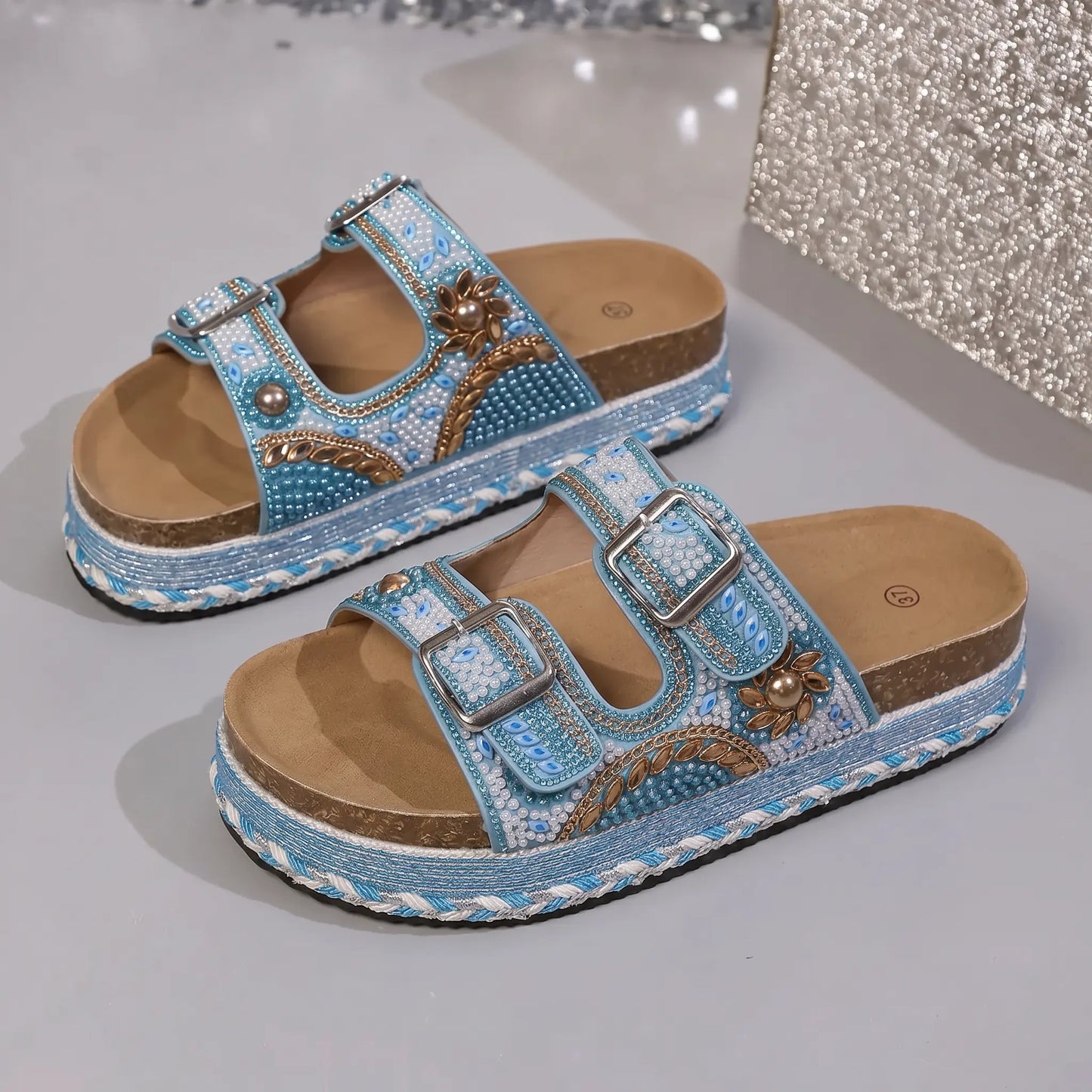 Sky blue Xylos platform slide sandals with intricate bead and sequin embellishments, featuring double adjustable buckle straps and a braided cork-effect sole.
