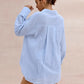 Back view of a woman wearing a light sky blue textured cotton oversized shirt with a camp collar and pearl buttons, against a blush pink background.