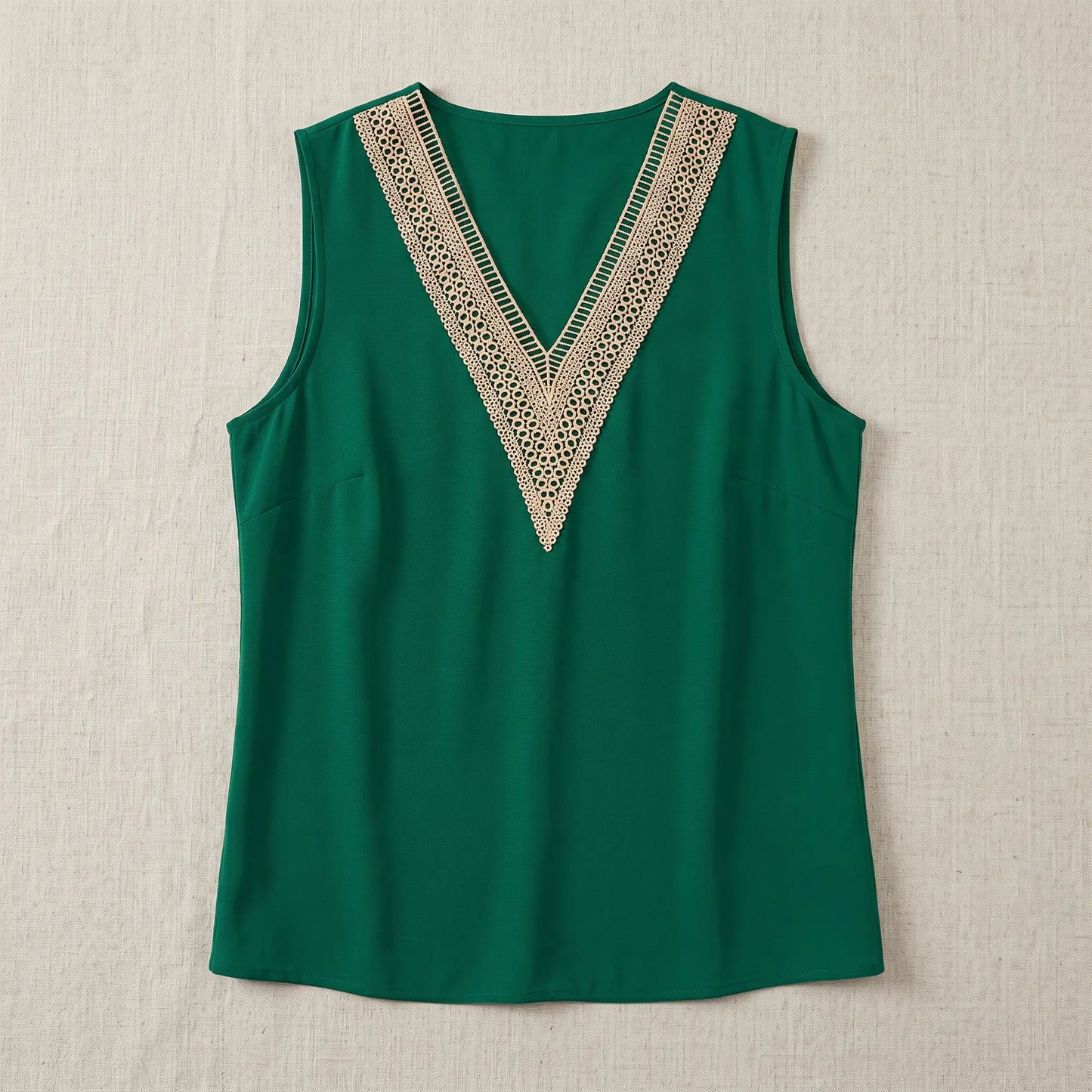 Sleeveless emerald green V-neck blouse with wide contrasting beige geometric crochet lace trim. Features clean armholes and a straight hem. Front view.