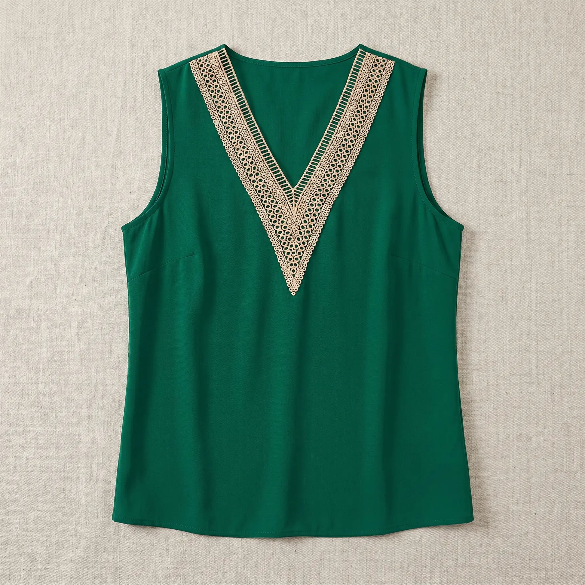 Sleeveless emerald green V-neck blouse with wide contrasting beige geometric crochet lace trim. Features clean armholes and a straight hem. Front view.