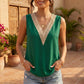Model wearing a sleeveless emerald green blouse with a deep V-neck featuring wide, contrasting beige crochet lace trim, styled casually with denim shorts and layered gold necklaces.