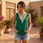 A woman poses outdoors in a green sleeveless blouse featuring a decorative cream crochet V-neck trim, paired with denim shorts.
