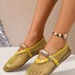 A pair of bright yellow mesh flat sandals with patent faux leather trim and decorative metallic oval buckles, shown on a woman's feet with a beaded anklet. The airy design is perfect for summer.