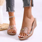 Elegant Sorani clear strap wedge sandals worn by a model, featuring a single transparent PVC strap with a gold pearl-like embellishment and a beige wedge heel on a white background.