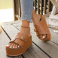 Tan platform slide sandals adorned with gold studs and an adjustable buckle, worn by a model on a wooden deck.