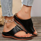 Black PU leather casual slip-on slides with toe-post design worn by a woman wearing ripped jeans and a beaded anklet on a wooden floor.