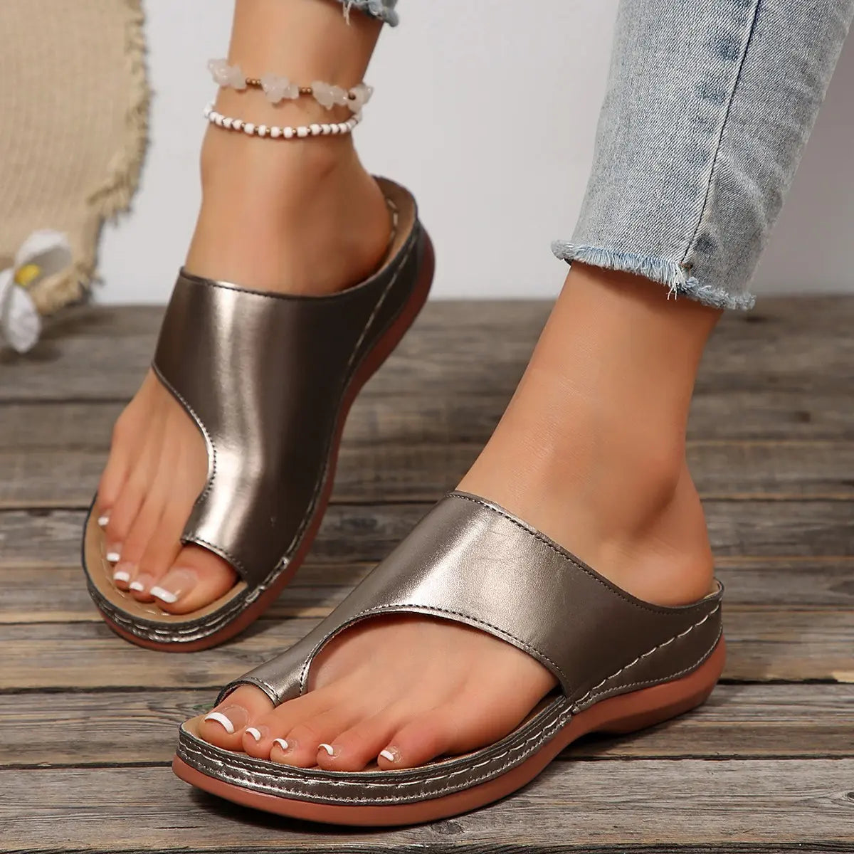 Women's metallic pewter-grey casual slip-on slides with a toe-post design and contoured footbed, shown on feet wearing distressed denim.