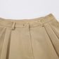 Close-up of warm khaki tailored Bermuda shorts featuring a high waist, button closure, and soft front pleats.