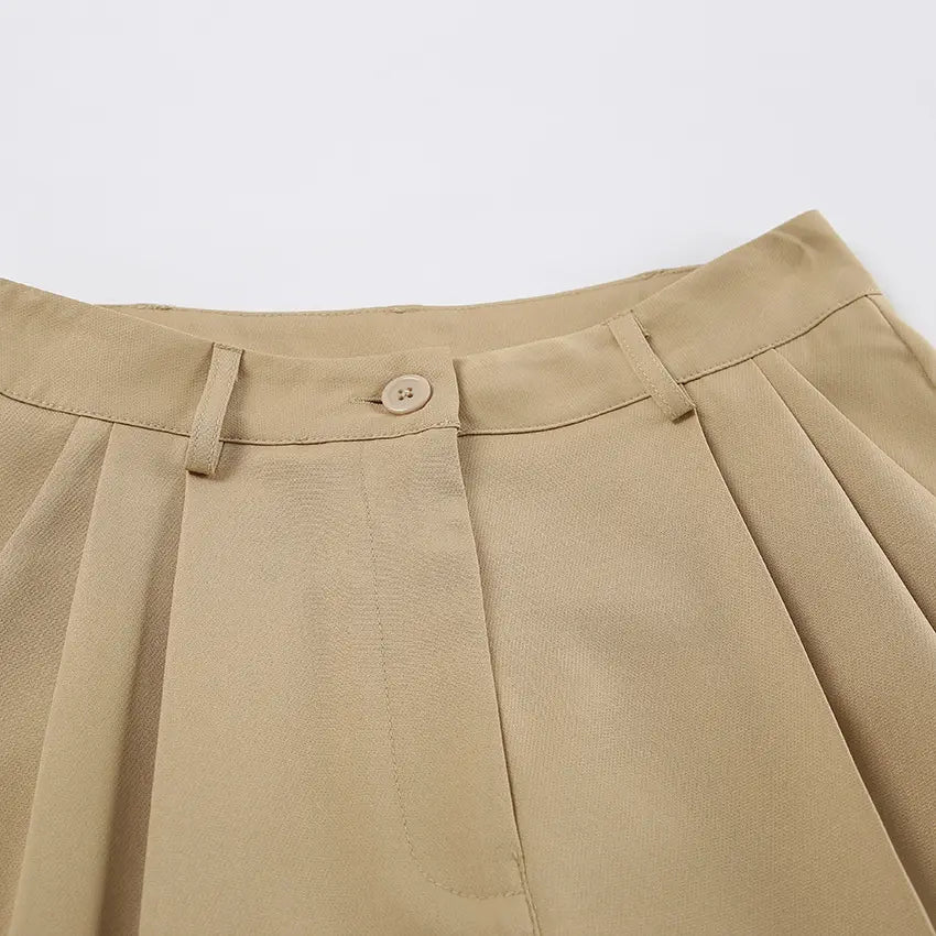 Close-up of warm khaki tailored Bermuda shorts featuring a high waist, button closure, and soft front pleats.