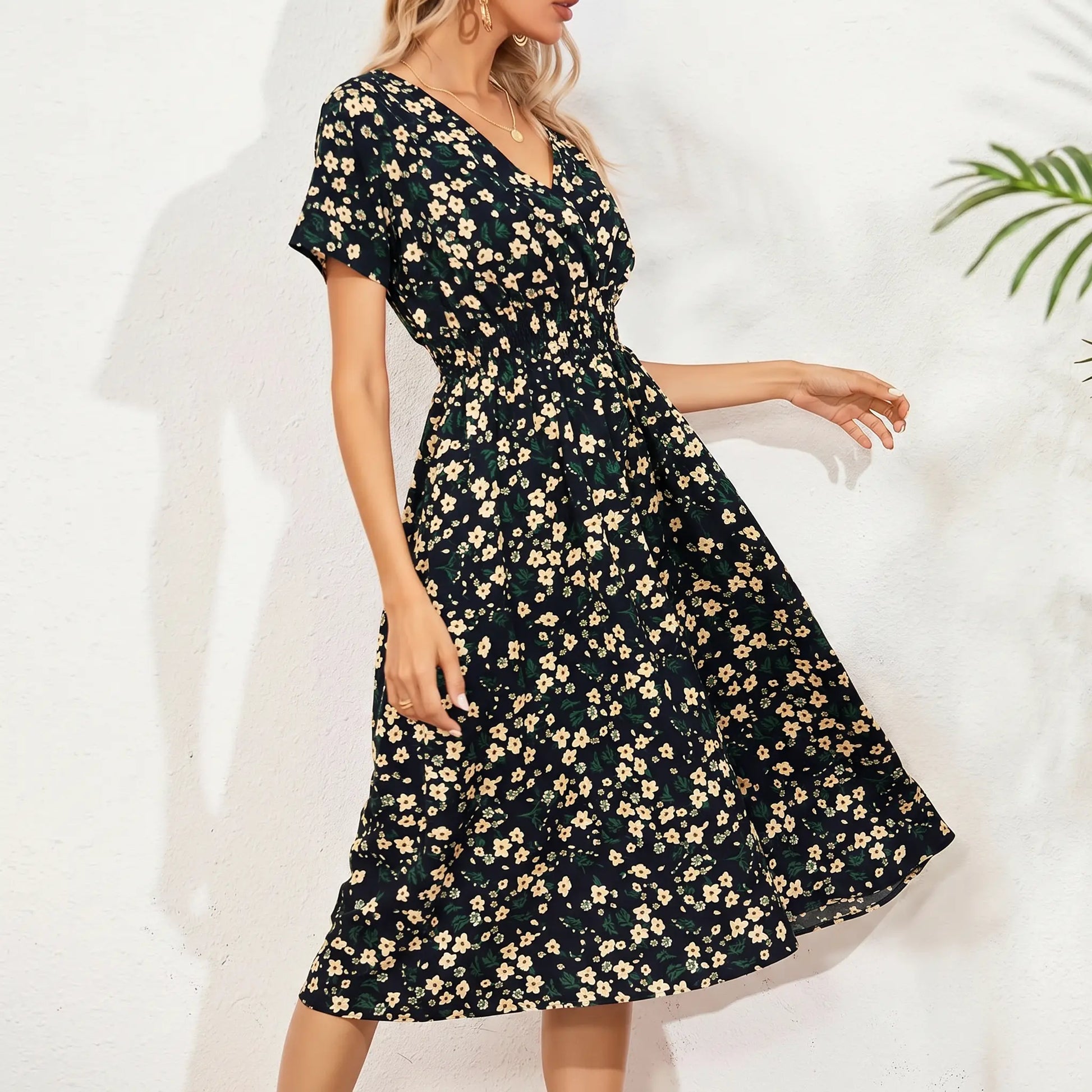 A woman models a V-neck midi dress in the 'Midnight Bloom' ditsy floral print, featuring short flutter sleeves and a cinched smocked waist, set against a textured white background with plant shadow.